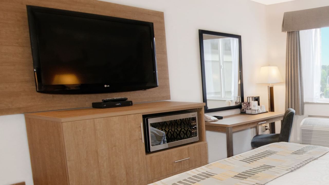 Hotel room with TV, microwave, bed, mirror, chair, and desk