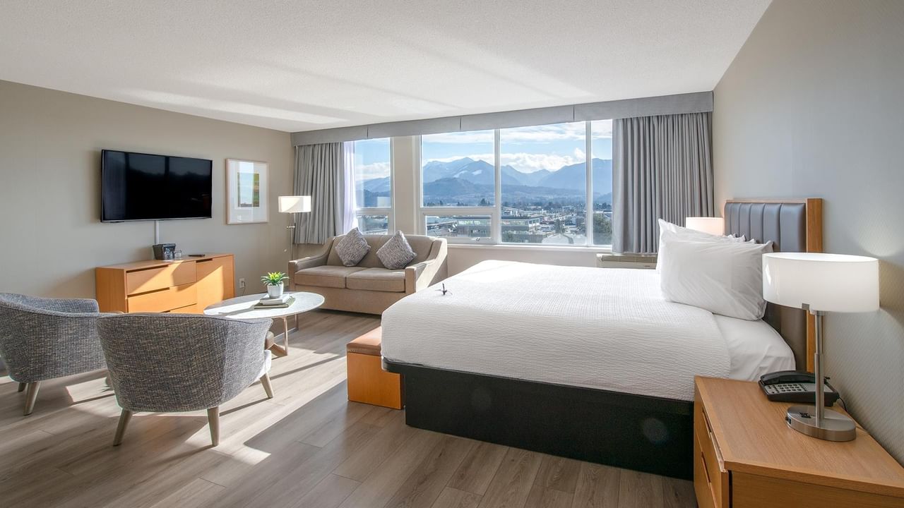 A comfortable hotel room with a bed, armchairs, and a view of mountains.