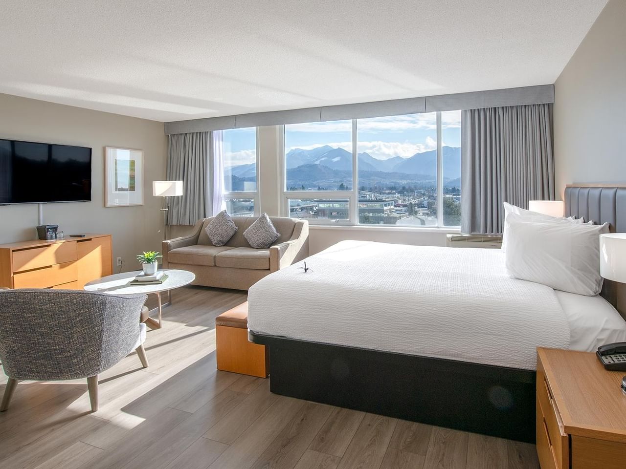 A comfortable hotel room with a bed, armchairs, and a view of mountains.