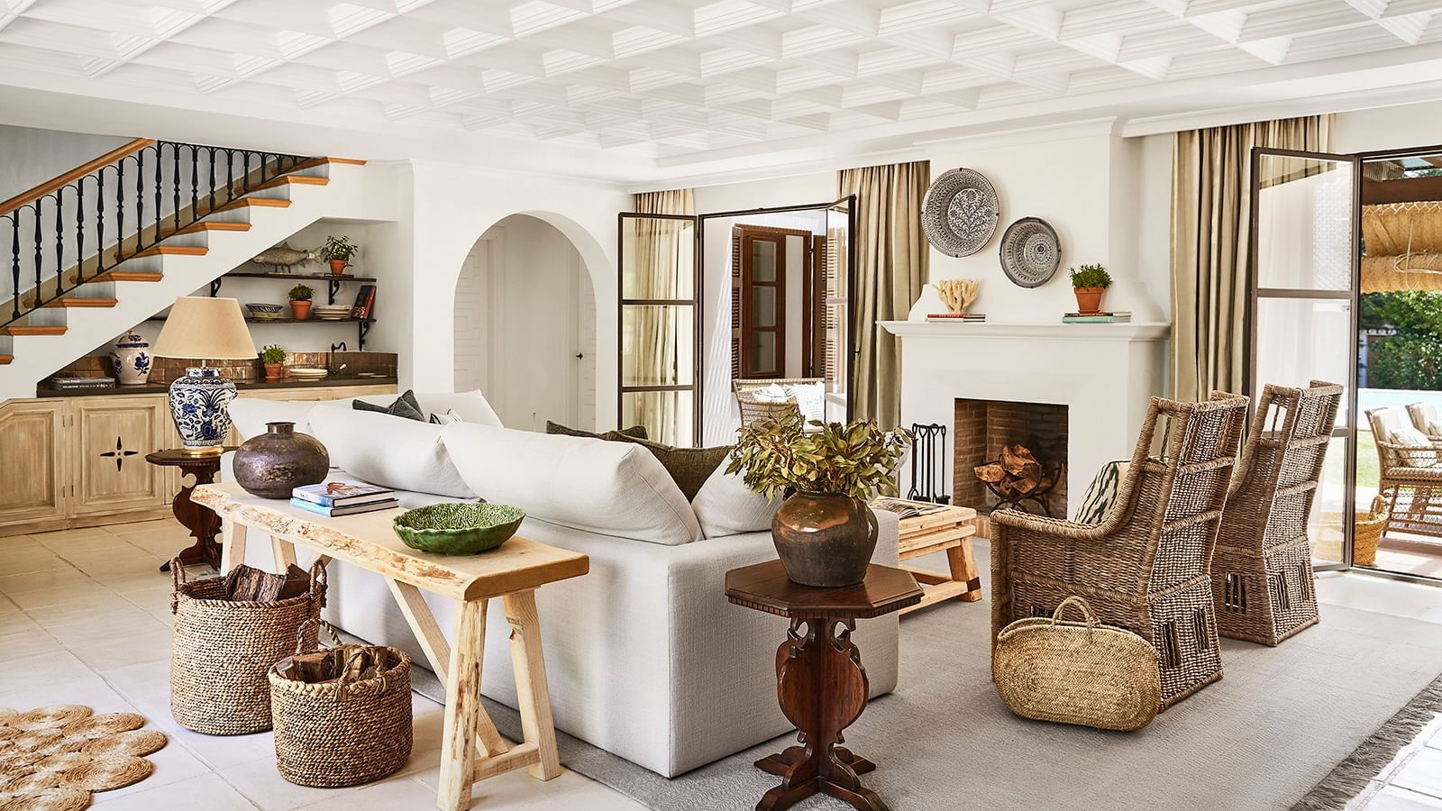 Living area with a white sofa and wicker chairs placed by a fireplace near a staircase at the Marbella Club
