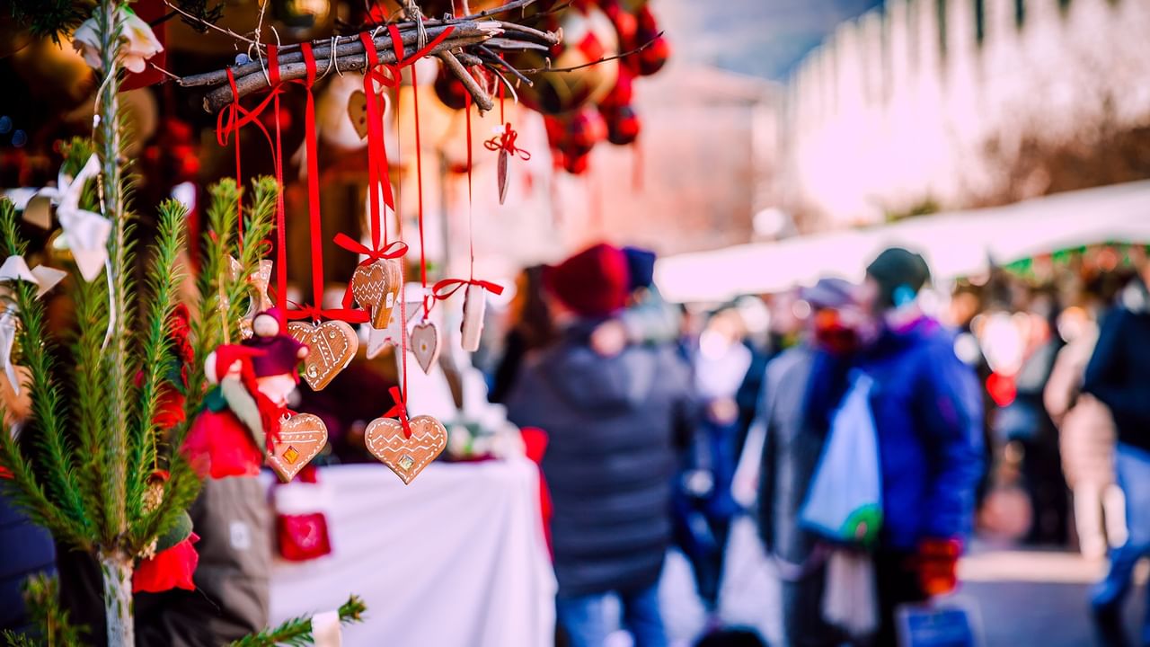 Handmade ornaments and festive decorations displayed at an outdoor holiday market with shoppers browsing vendor stalls.