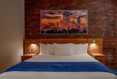 Bed between the sidetables and skyline art above the exposed brick wall in King City View at Harborside Inn Boston