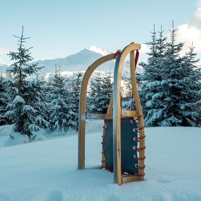 Wooden sled stands in fresh snow with a mountain backdrop under a clear sky near Falkensteiner Hotels & Residences