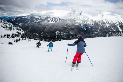 Lady & two kids gliding down a snowy slope on skis near Blackcomb Springs Suites