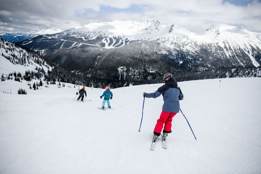 Lady and two kids skiing down a snowy slope near Blackcomb Springs Suites