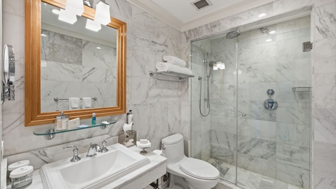 Deluxe King bathroom with marble walls, glass shower, wood-framed mirror, and white vanity at el PRADO Hotel, Palo Alto.