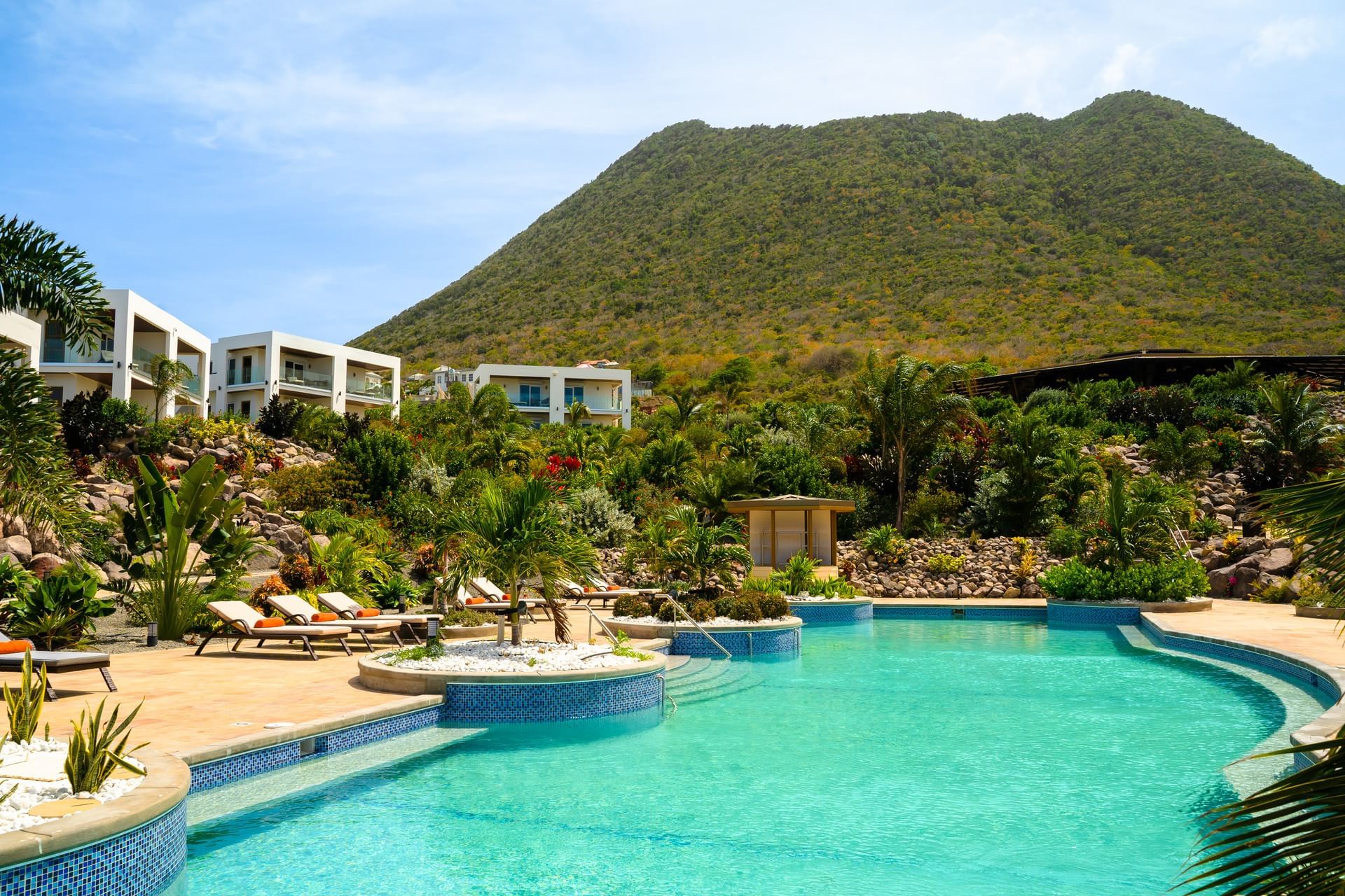 Hibiscus Pool, surrounded by lush greenery and modern villas, with a scenic mountain backdrop at Golden Rock Resort