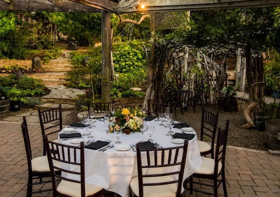 Outdoor garden dining table set with white linens and floral centerpiece under rustic pergola at Cambria Pines Lodge