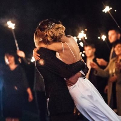 bride and groom hugging with wedding guests holding sparklers surrounding them