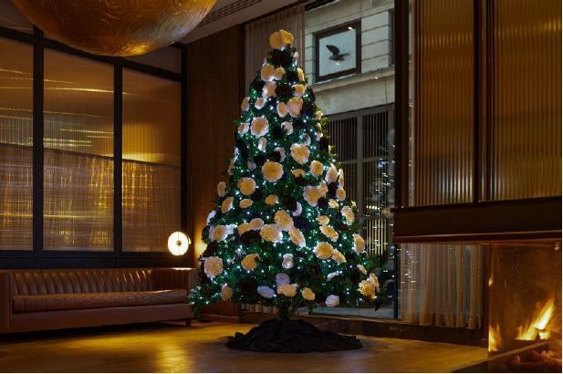 Beautifully decorated Christmas tree with glowing lights and yellow ornaments, standing in the festive lobby of The Londoner