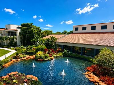 Landscaped fountain pond with tropical flowers and ornamental rocks beside red tile roof buildings at Miami Lakes Hotel
