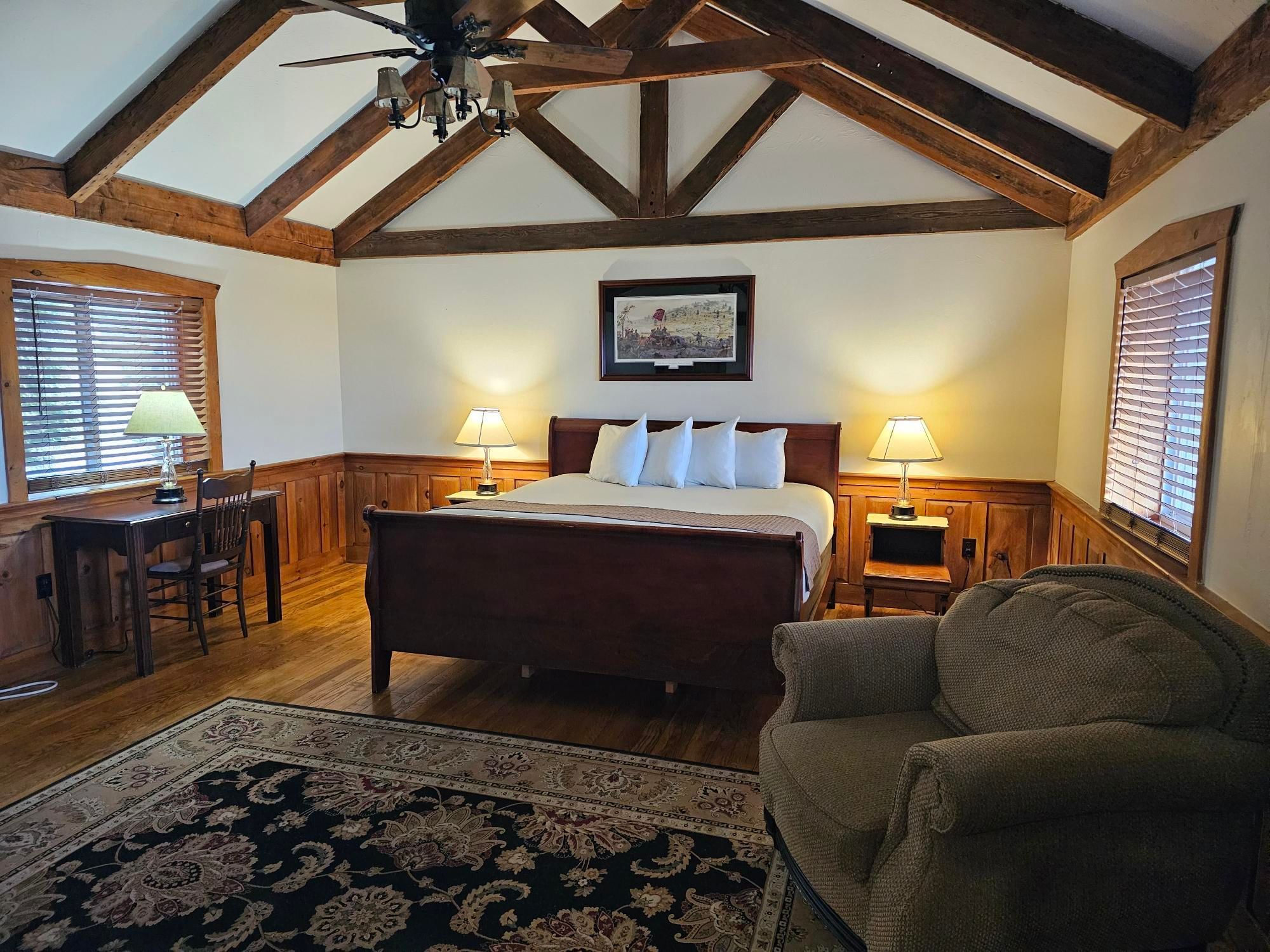 Captain's Lodge cozy bedroom with wooden furniture, a king bed, two lamps, and a chair at The Lodges at Gettysburg Hotel in PA.