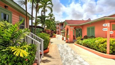 Sunny walkway between peach resort buildings with green shrubbery and tropical palm trees at Worthing Court Apartment