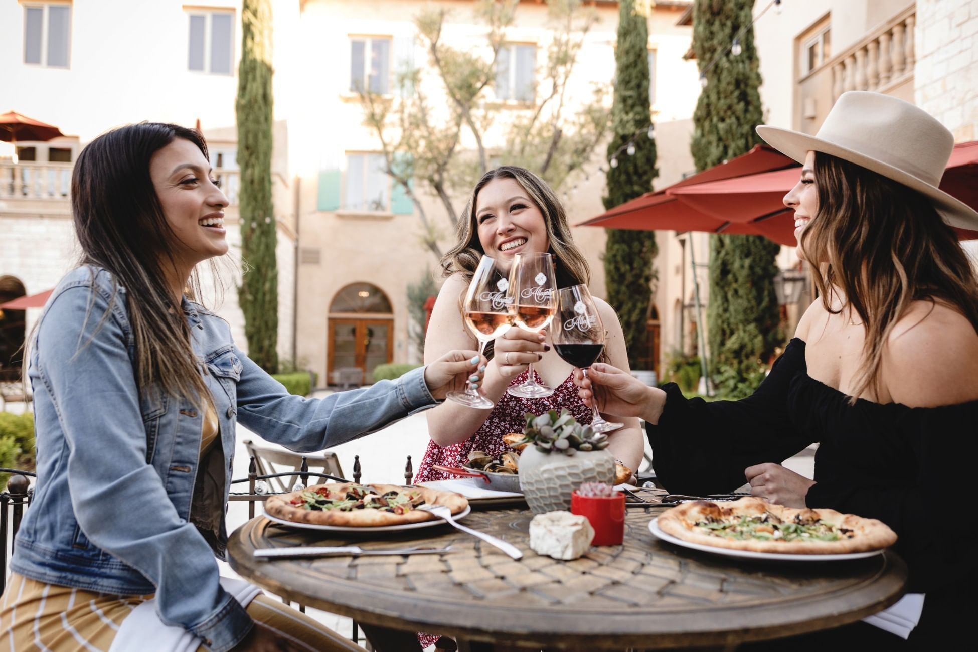 Thre women sitting around a small table, holding wine glasses and toasting