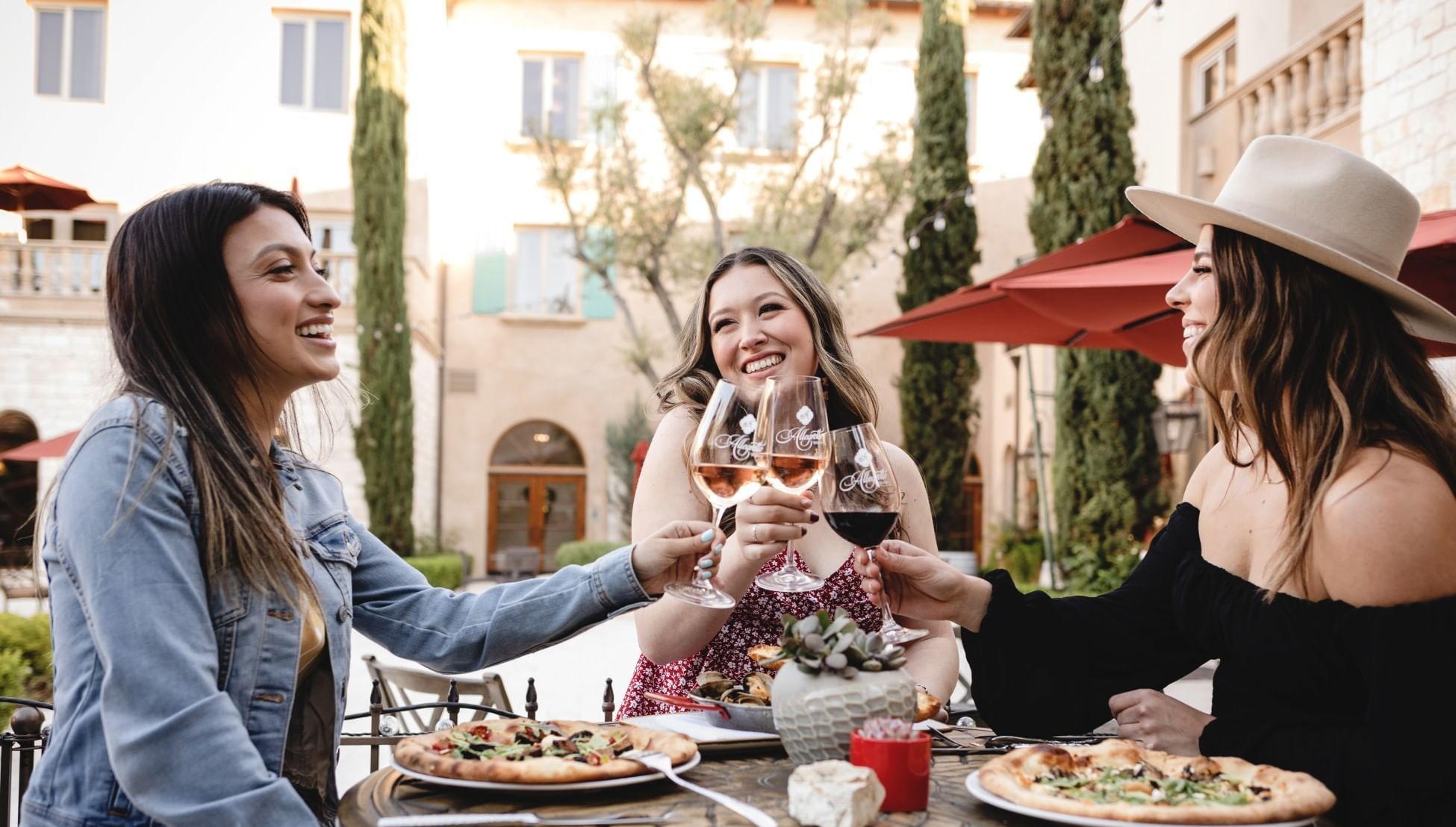 Thre women sitting around a small table, holding wine glasses and toasting