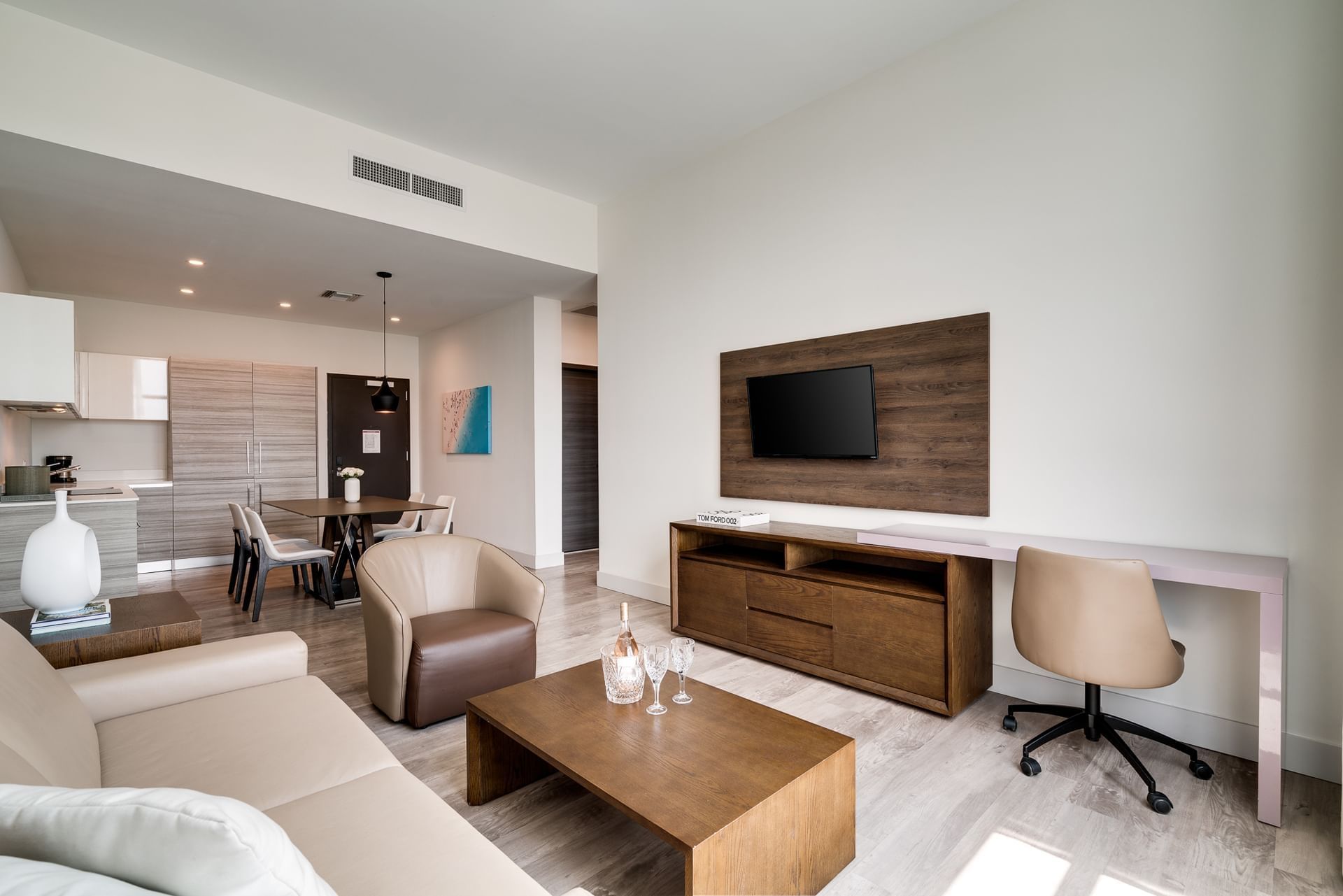 A modern living room with a sofa, coffee table, TV, desk, and kitchenette.