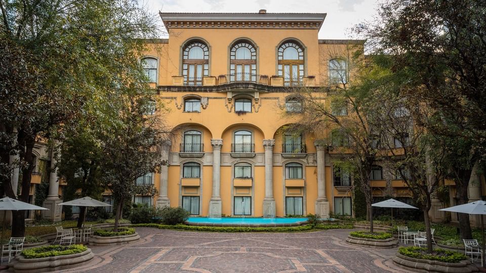 Majestic yellow facade overlooking a paved courtyard with trees and blue pool at Quinta Real Monterrey