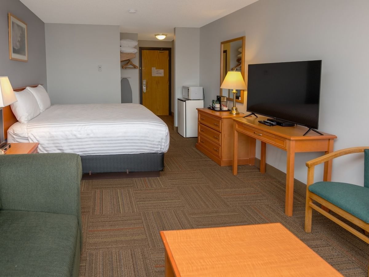 Hotel room with bed, nightstand, dresser, flat-screen TV, desk, chair, couch, and coffee table.