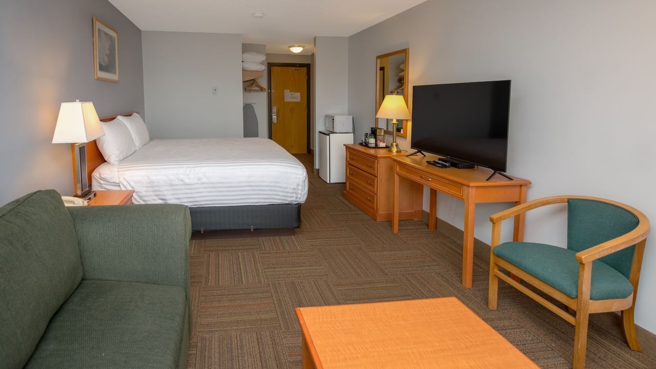 Hotel room with bed, nightstand, dresser, flat-screen TV, desk, chair, couch, and coffee table.
