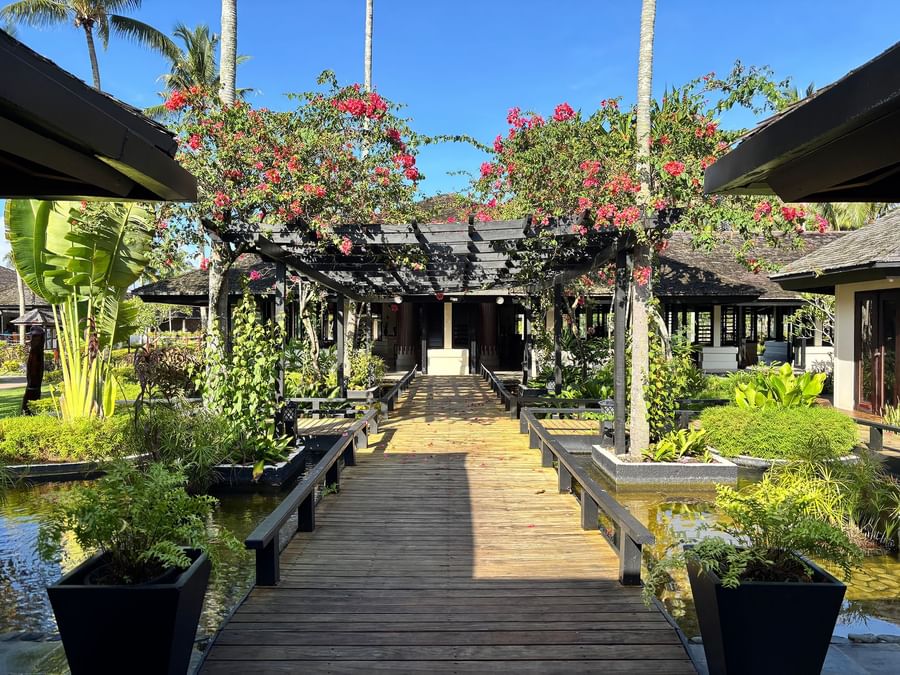 Wooden walkway bordered by plants and trees with red flowers at Warwick Le Lagon Vanuatu.