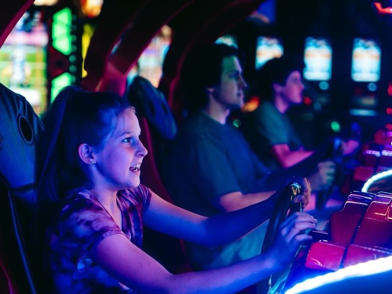 Niña jugando en un simulador de carreras en la sala de juegos de Fiesta Americana Funeeq con luces de neón y máquinas