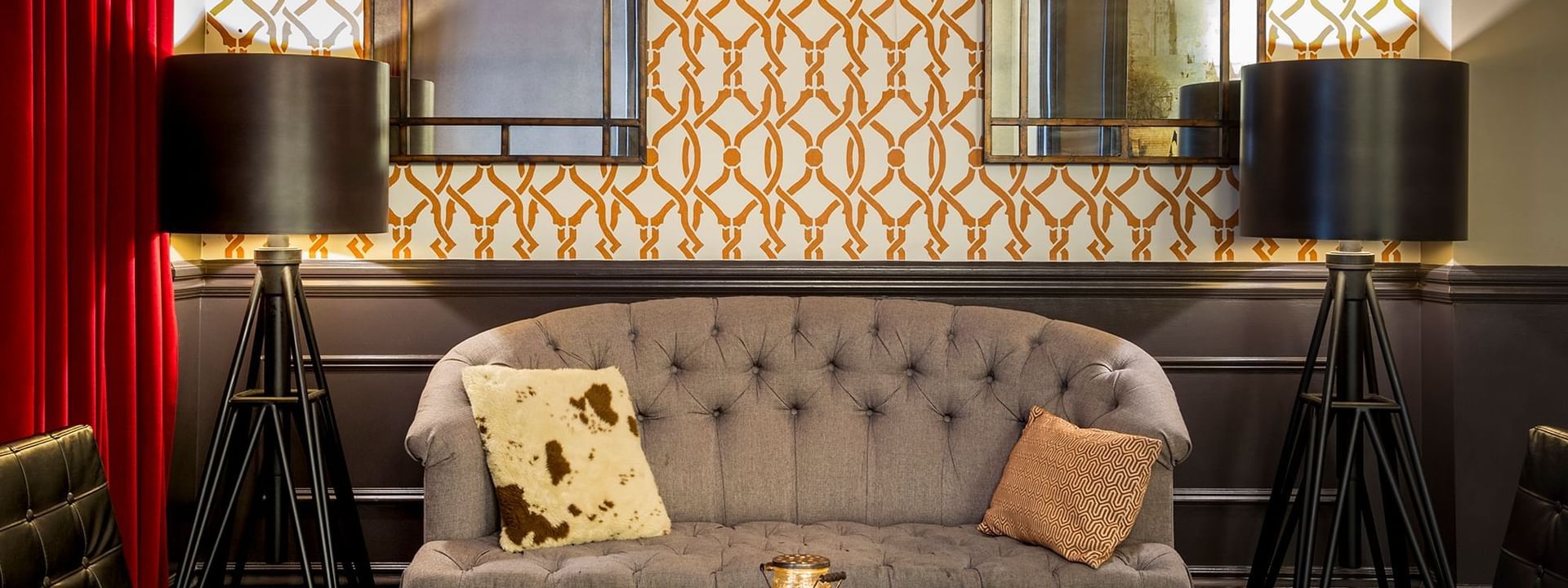 Grey tufted sofa by a wooden table and tripod lamps under a patterned wall in The European at Warwick San Francisco
