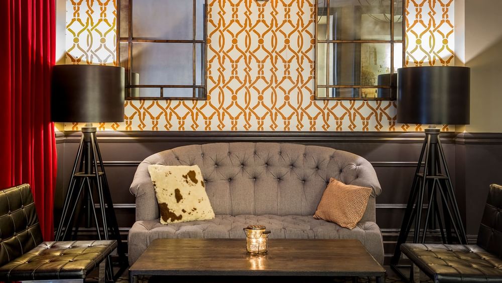 Grey tufted sofa by a wooden table and tripod lamps under a patterned wall in The European at Warwick San Francisco