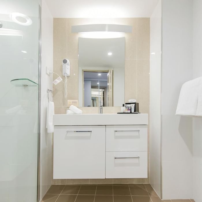 White tiled interior of a room bathroom with a shower cubical and vanity area at Mercure Charlestown
