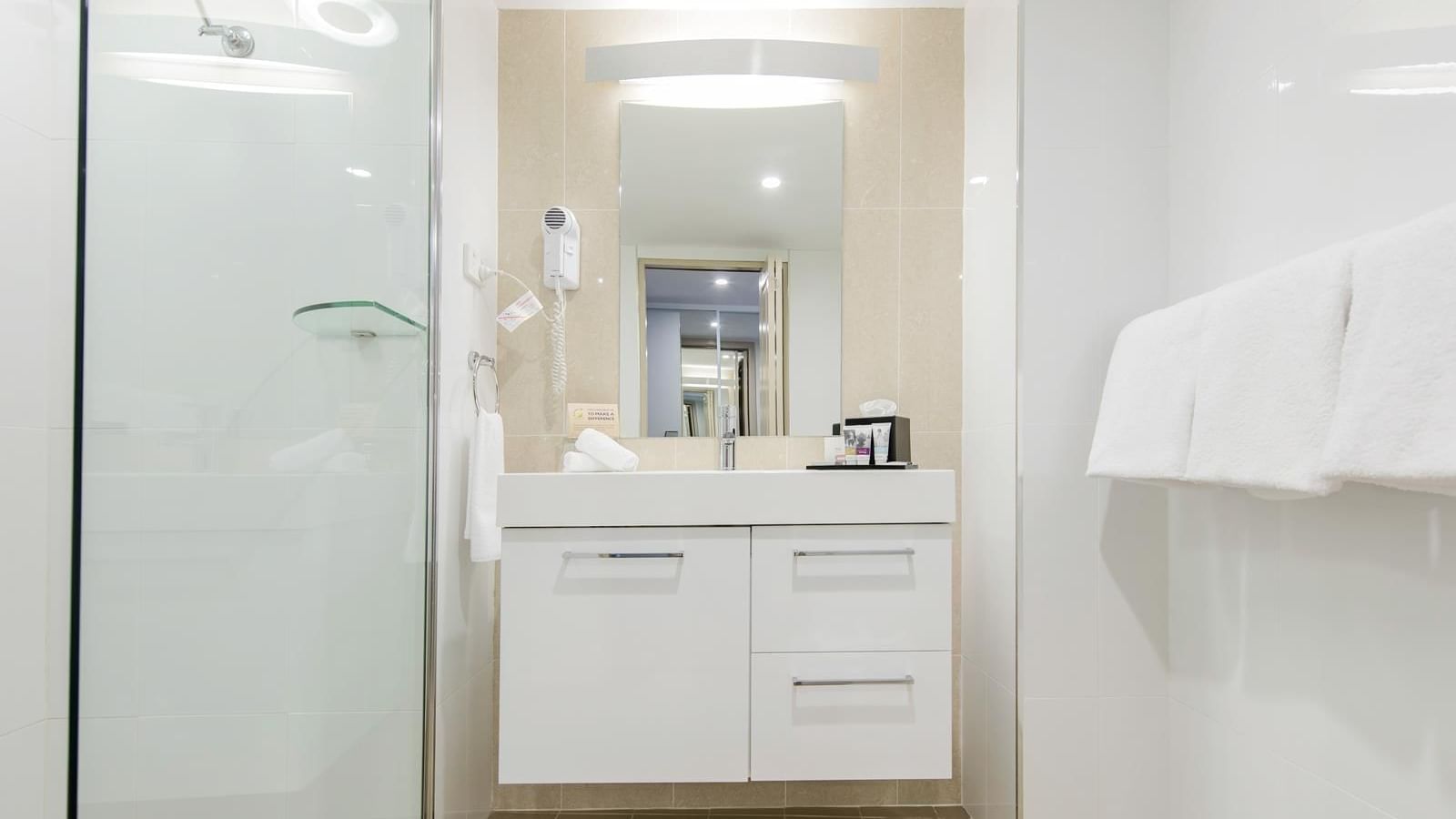 White tiled interior of a room bathroom with a shower cubical and vanity area at Mercure Charlestown