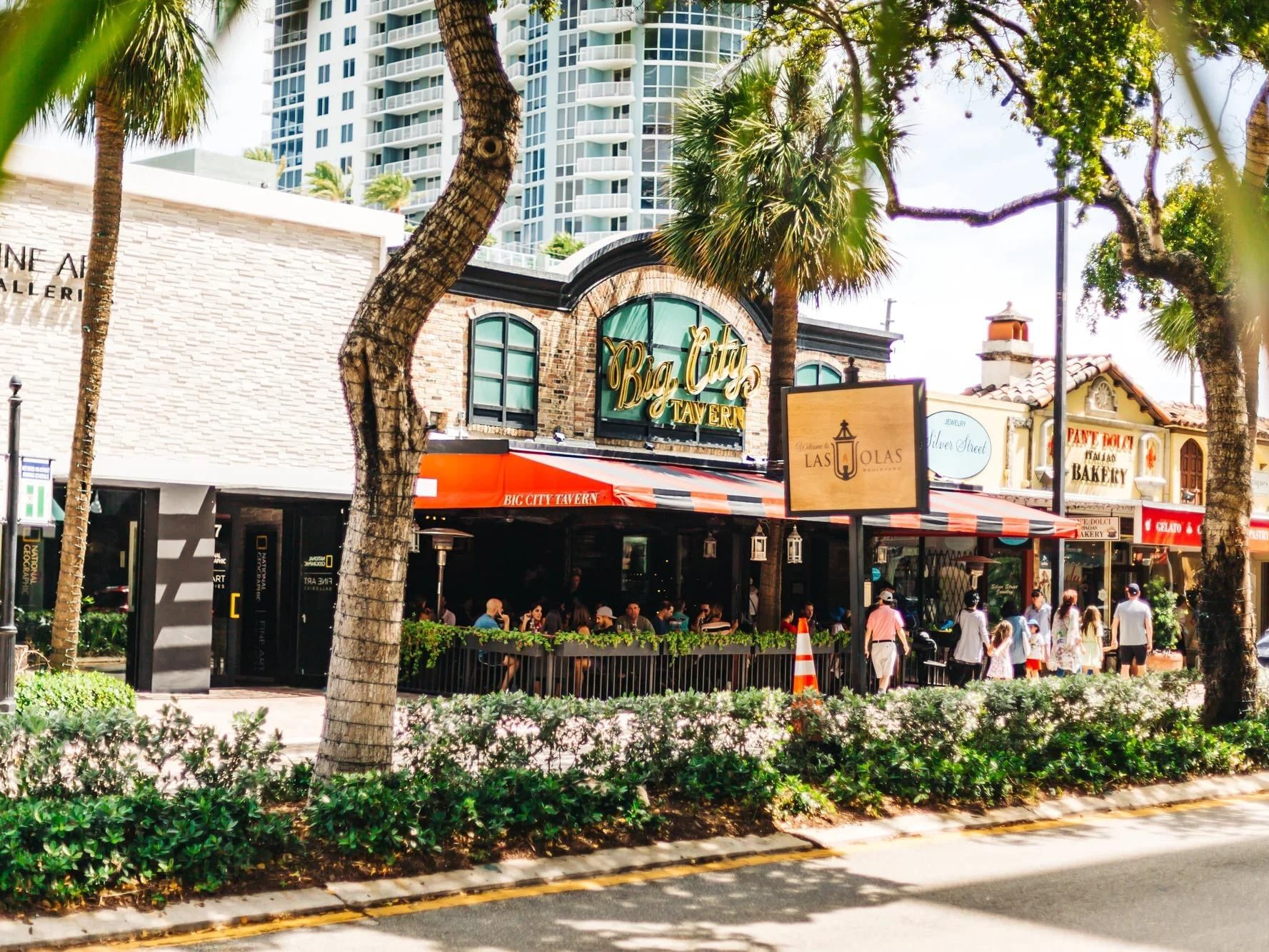 Vibrant street scene with palm trees, outdoor dining, and colorful storefronts on a sunny day in a coastal city