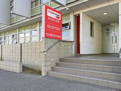 Red Student Living Auckland Anzac reception sign on building entrance with steps.