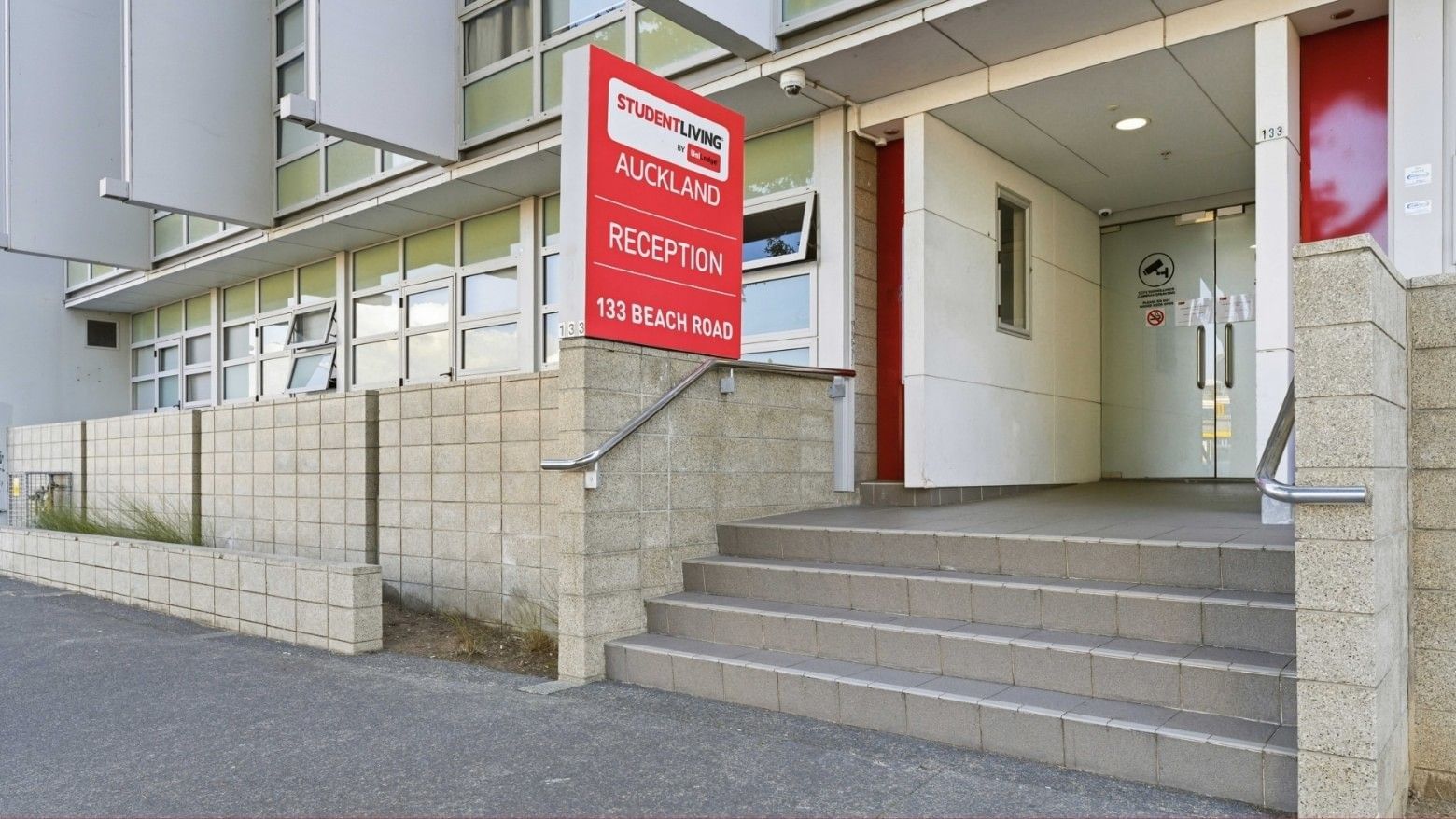 Red Student Living Auckland Anzac reception sign on building entrance with steps.