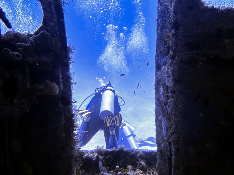 Diver by a dark wreck under the blue ocean surrounding tiny bubbles at Warwick Paradise Island Bahamas