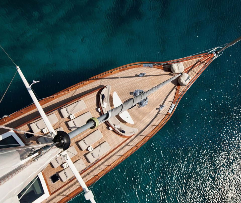 Top-down aerial view of a wooden yacht deck with plush sun loungers on deep blue sea water near Meraviglia