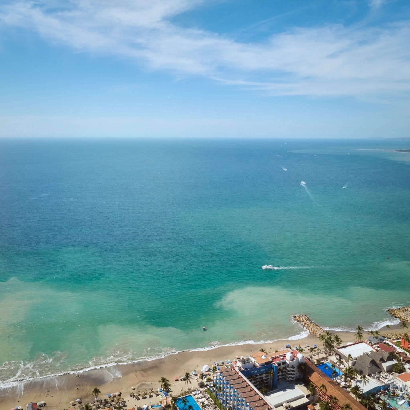 Vista aérea desde Hacienda Buenaventura Hotel mostrando la costa turquesa de Puerto Vallarta, playa de arena, olas del océano y un paisaje costero tradicional bajo un cielo azul despejado.