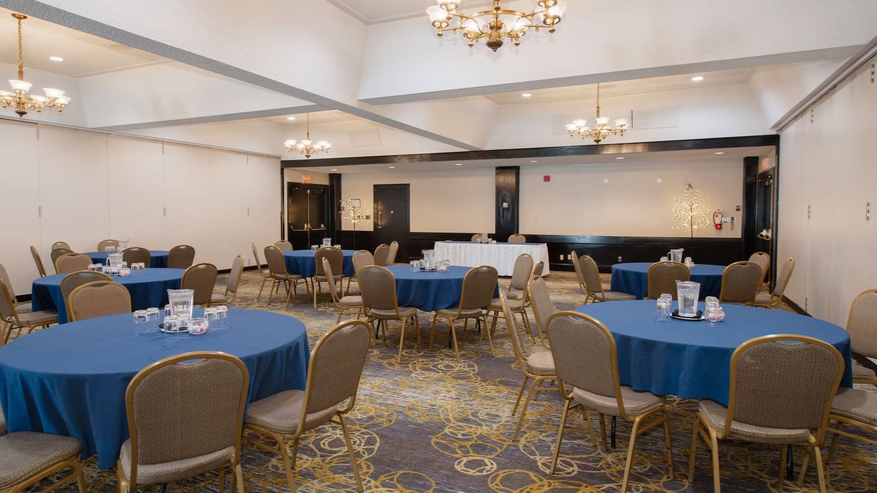 An meeting room with round tables, chairs, and chandeliers, set for an event.