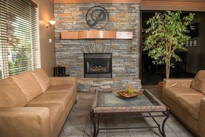 Leather sofas around a glass table with a stone fireplace in the inviting lobby at Hilltop Inn Salmon Arm