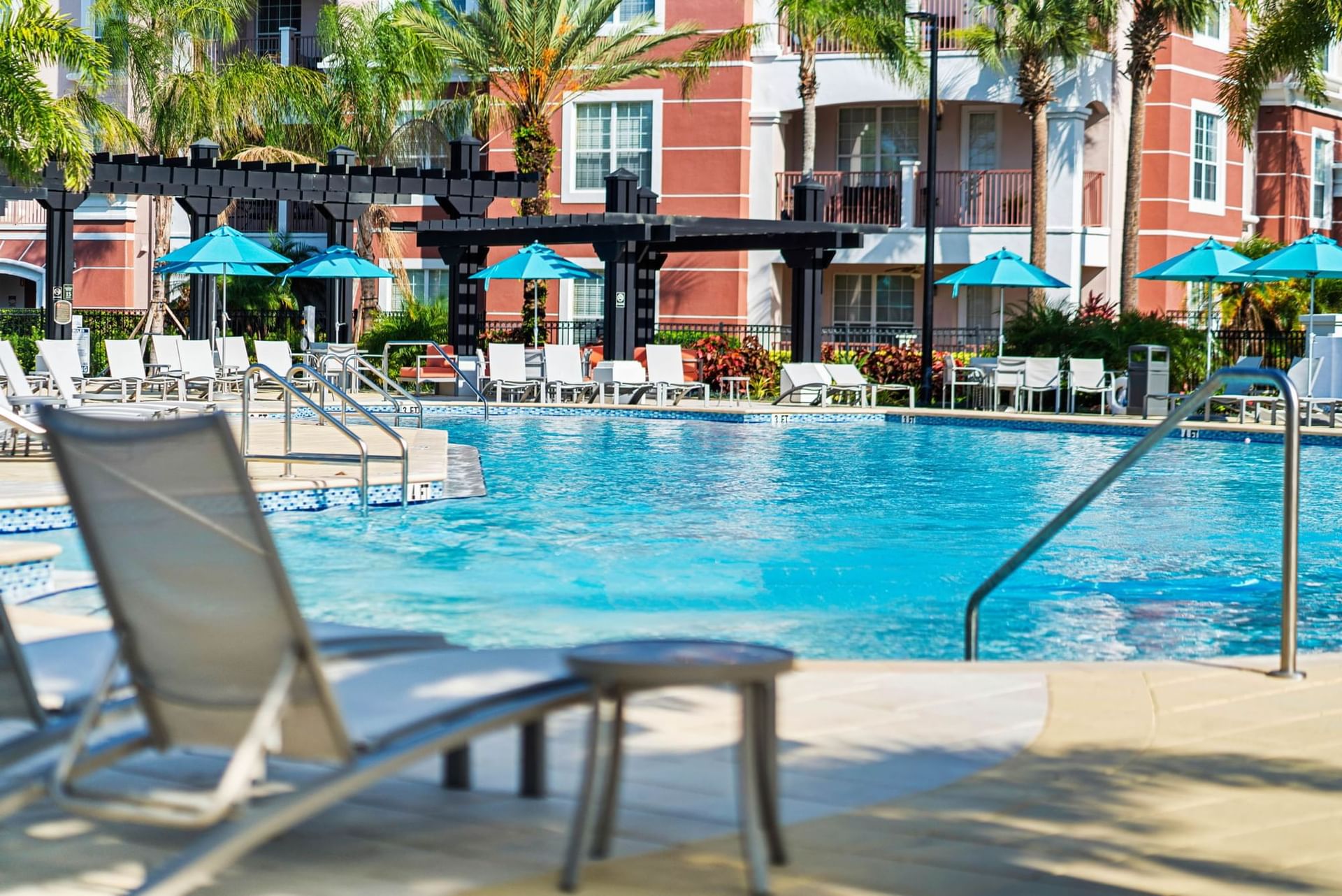 Poolside lounge chairs and tables with umbrellas at Vista Cay Resort By Millenium