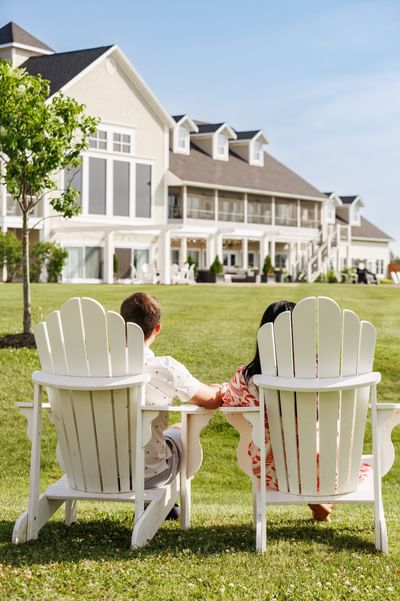 Back view of a couple sitting in white Adirondack chairs looking at the main building at Rodd Crowbush Golf & Beach Resort