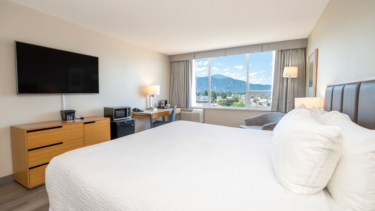 Accessible hotel room with a large king bed, desk, TV, and window showing mountains.