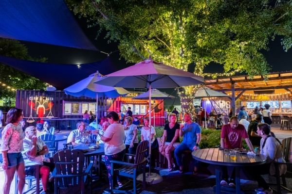 At night, groups of people sit around tables with open umbrellas. In the background, shipping containers converted into food counters are illuminated. A visit to Boxi Park is a great thing to do near MCO.