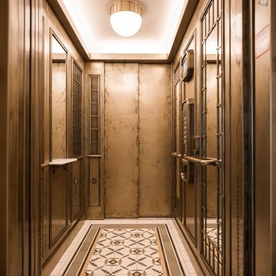 Elegant vintage elevator with gold-toned walls, decorative mirrors, and a patterned tiled floor at Hotel Motto Vienna
