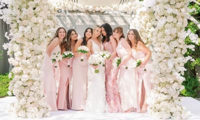 Bride & bridesmaids posing by a floral arch in a ballroom at Luxe Sunset Boulevard Hotel