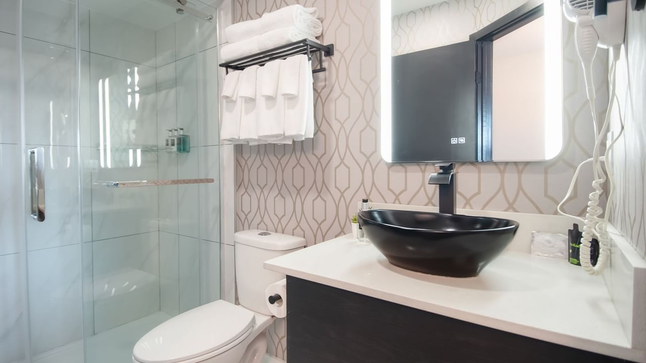 Hotel bathroom with toilet, sink, mirror, shower, towels and soap