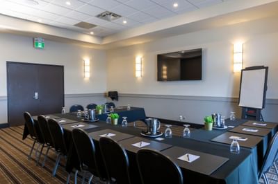 Meeting room setup with black chairs by long tables under a flat-TV in Southwest Miramichi Room at Rodd Miramichi River