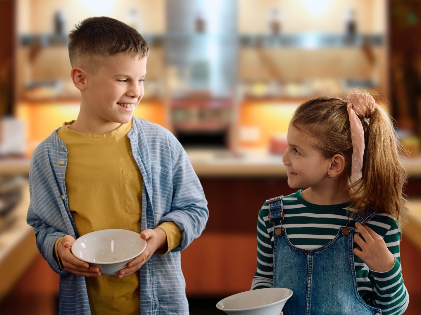 Two smiling children holding bowls at the vibrant breakfast buffet at Amora Brisbane Hotel