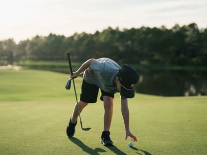 Golfer placing ball on green with putter and wooded backdrop at Camp Creek Inn in Inlet Beach