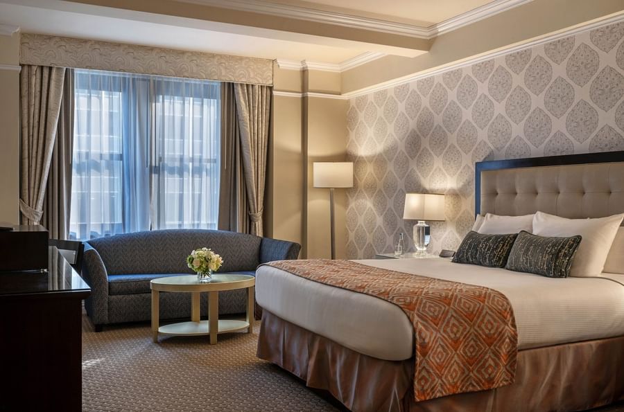 Elegant hotel room with large bed, couch, and flower vase at Warwick New York.