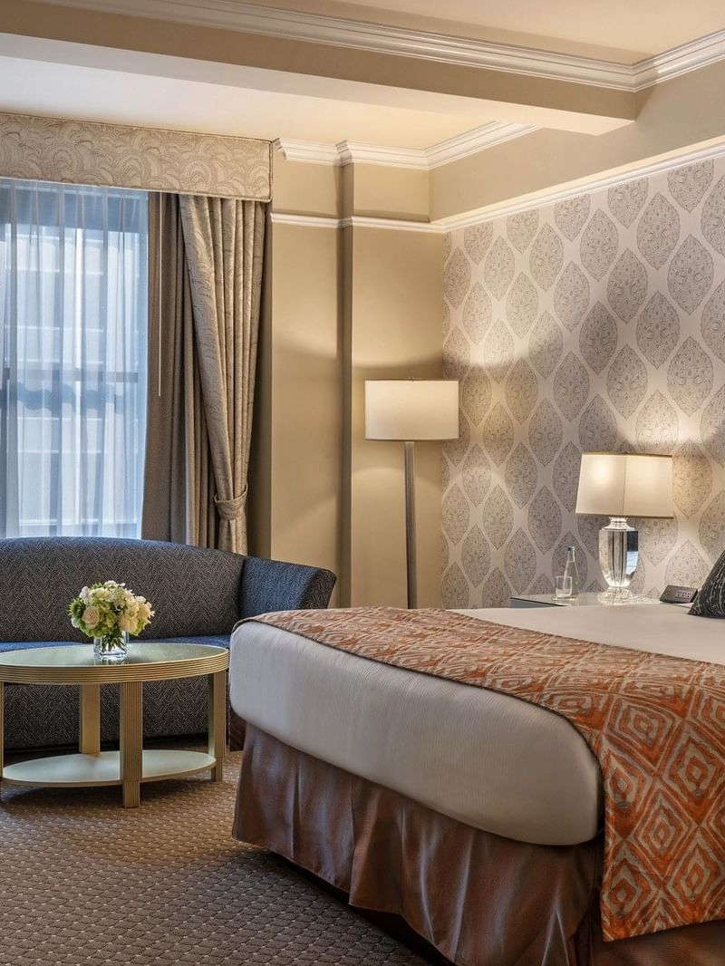 Bed with Patterned accent wall & blue sofa, and large curtained window in Junior Suite at Warwick New York