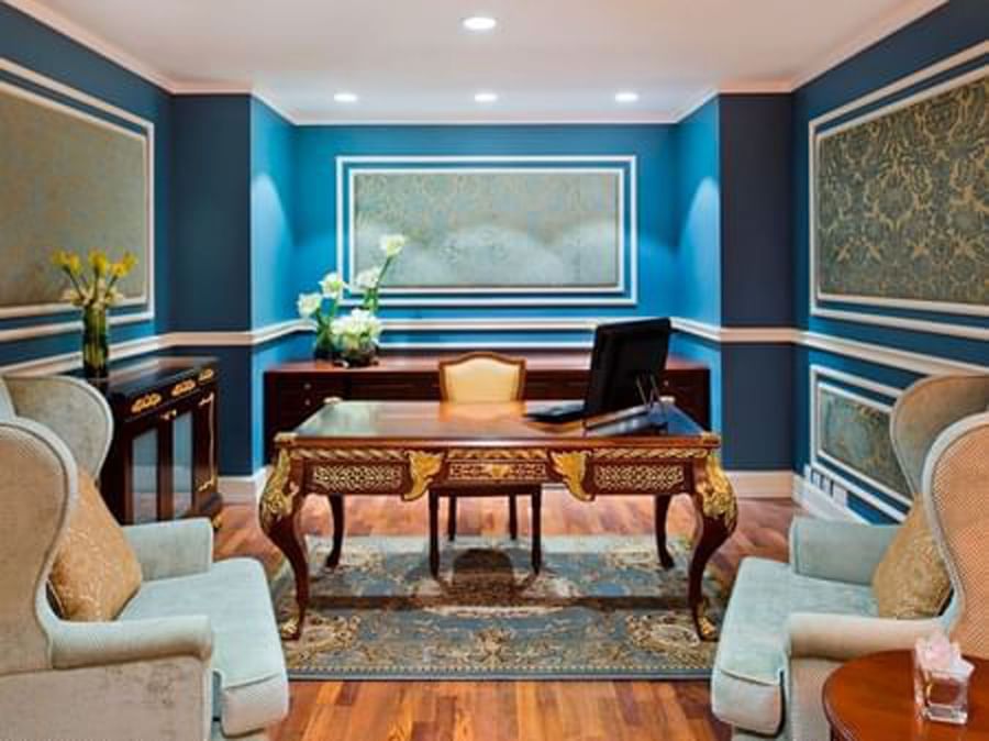 Coral Room features a wood desk and wingback chairs under a blue wall at Warwick Doha Hotel